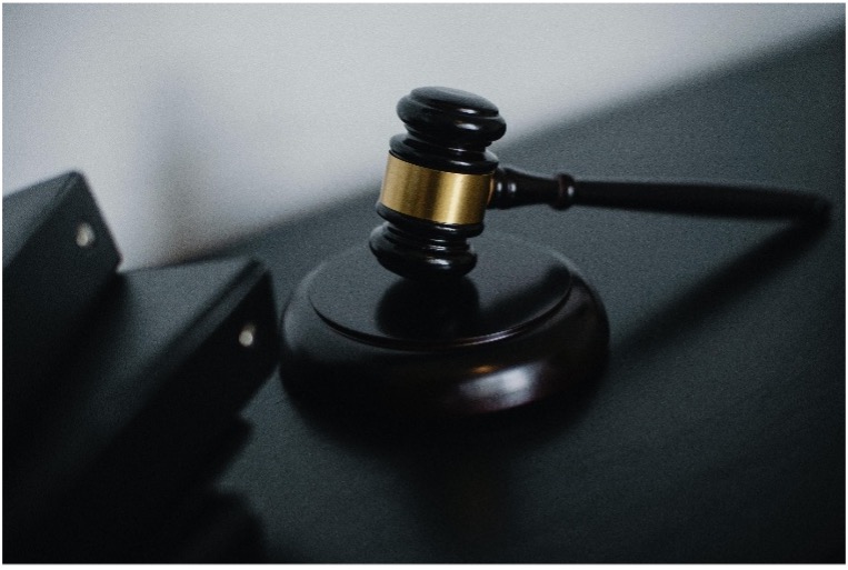 Ein Gerichtshammer liegt auf einem schwarzen Tisch neben zwei Aktenordnern